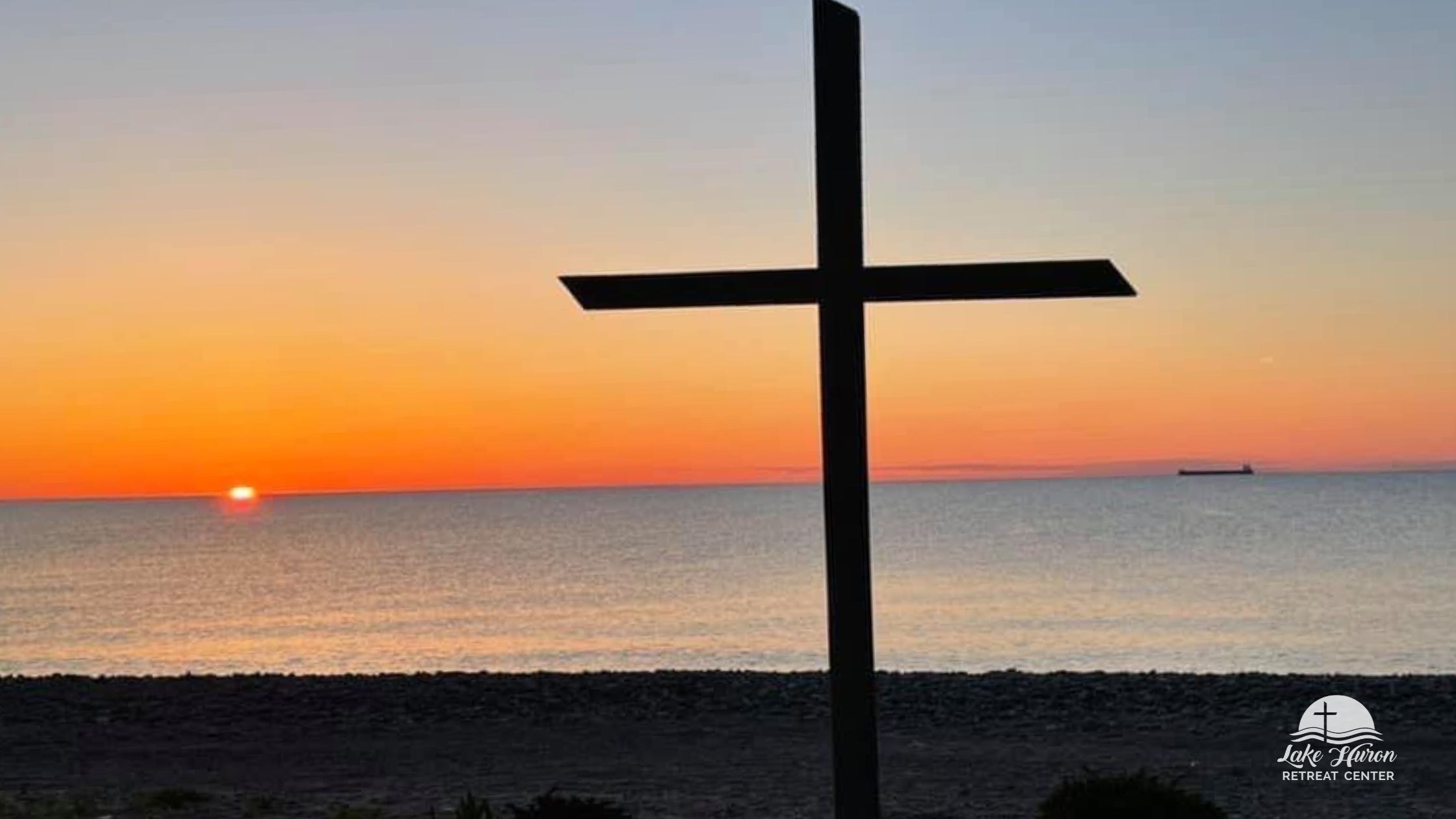 Orange sunrise over Lake Huron with the cross silhouetted at Lake Huron Retreat Center.