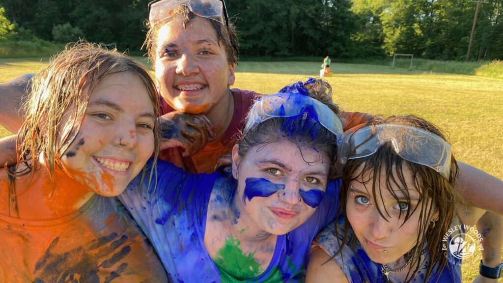 Four teens with paint playfully all overthemselves from a game.