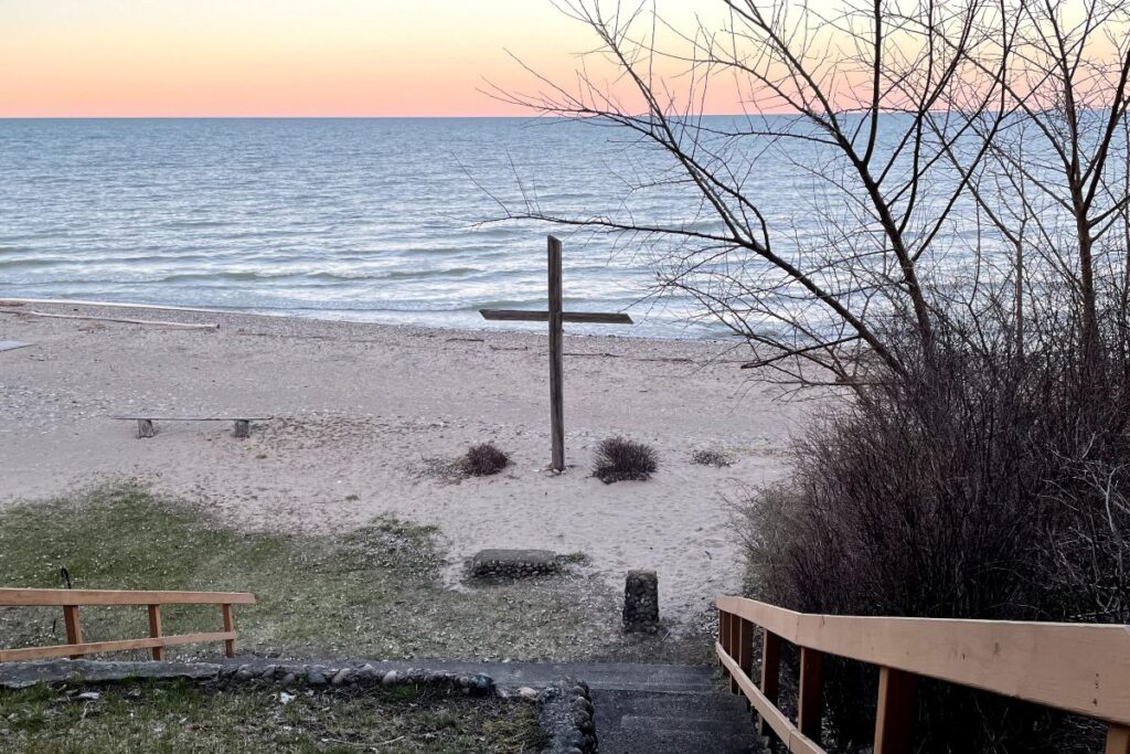 sunrising over Lake Huron with a large wooden cross on the beach. 