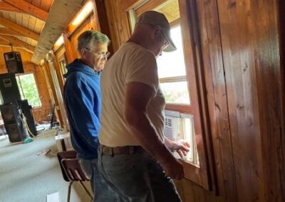 two workers installing a window airconditioner in a wood-paneled room